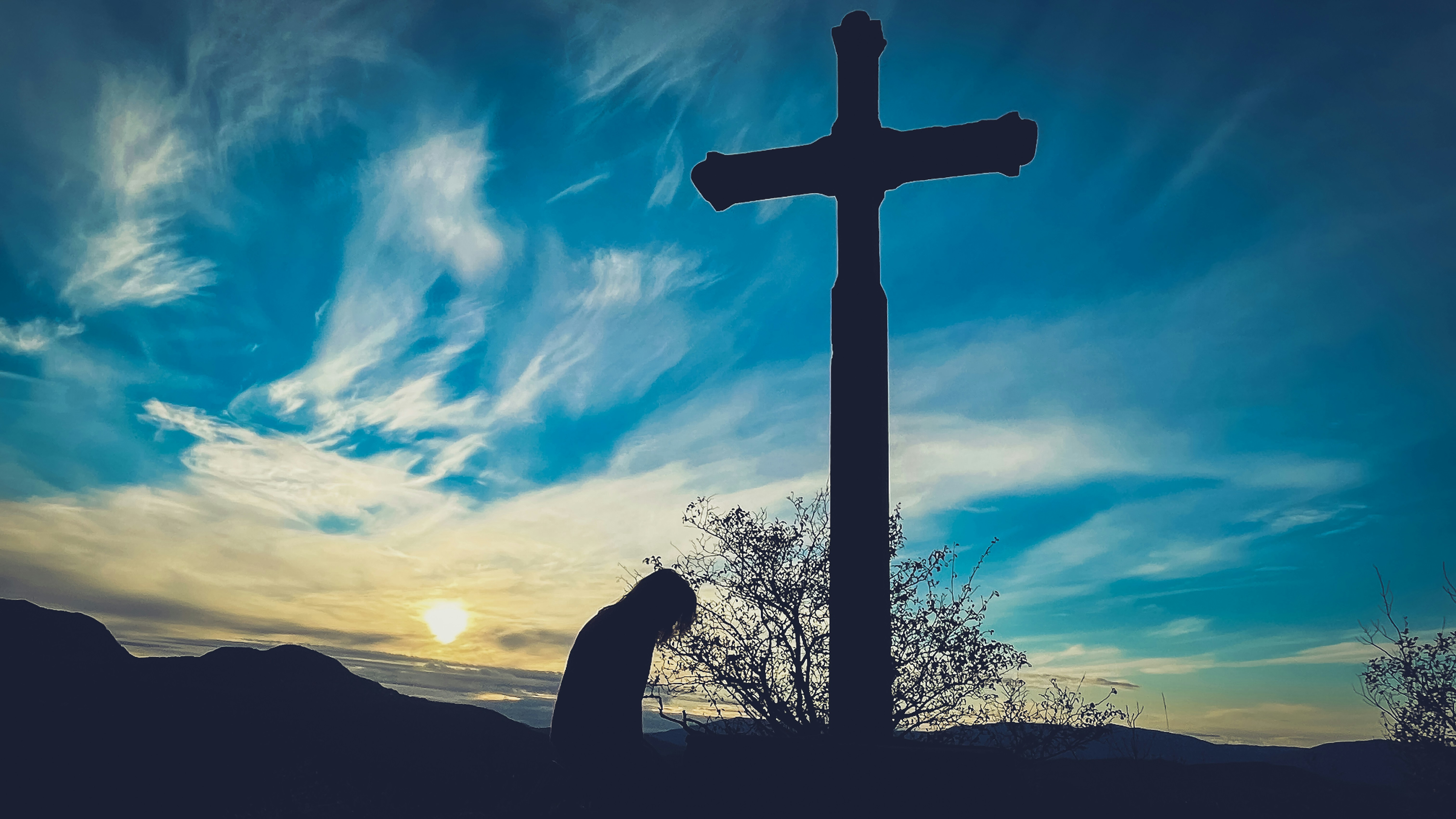 A person praying for frogiveness in front of a raised cross on a high open field