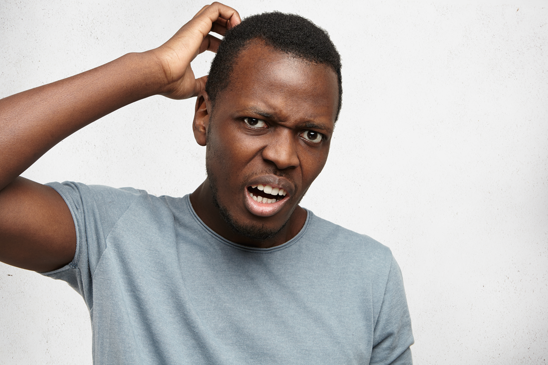 An African American man in gray t-shirt looking with a confused and puzzled expression, scratching his head