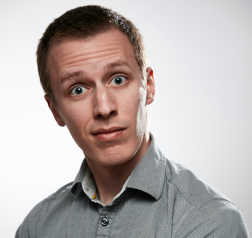 A man in a gray button-up shirt in a surprised facial expression